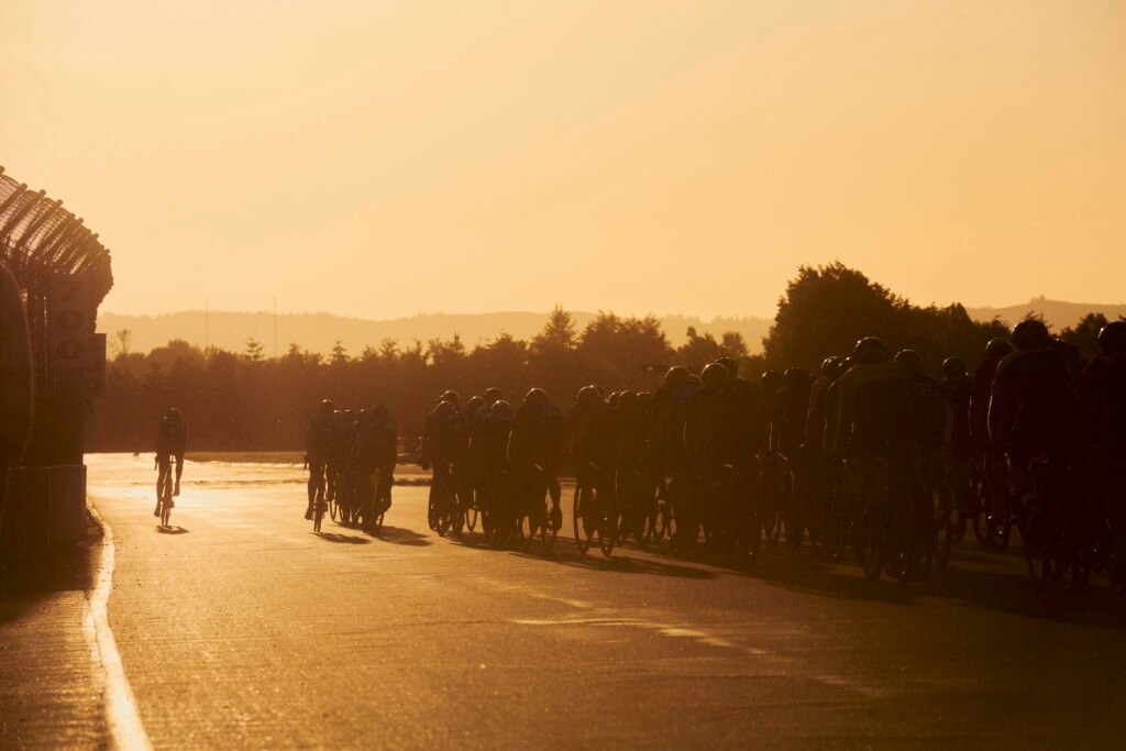 A field of cyclists race on the Portland International Raceway as the sun sets